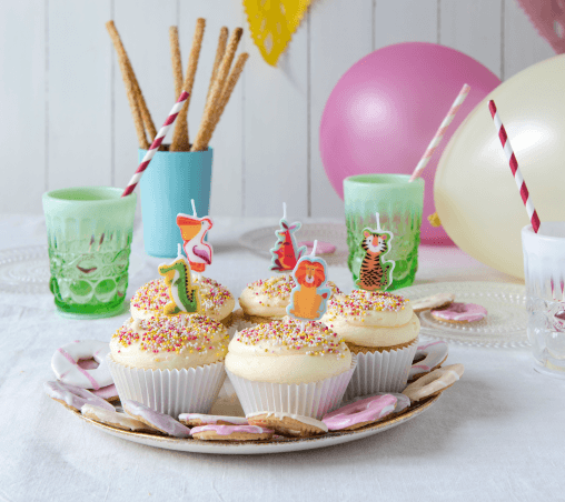 Image of a kids party table set up. In the forefront is a plate of 5 cupcakes with animal candles in them.