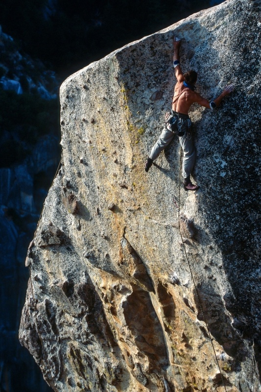 A rock climber high up on a tall vertical rock face, holding on tightly
