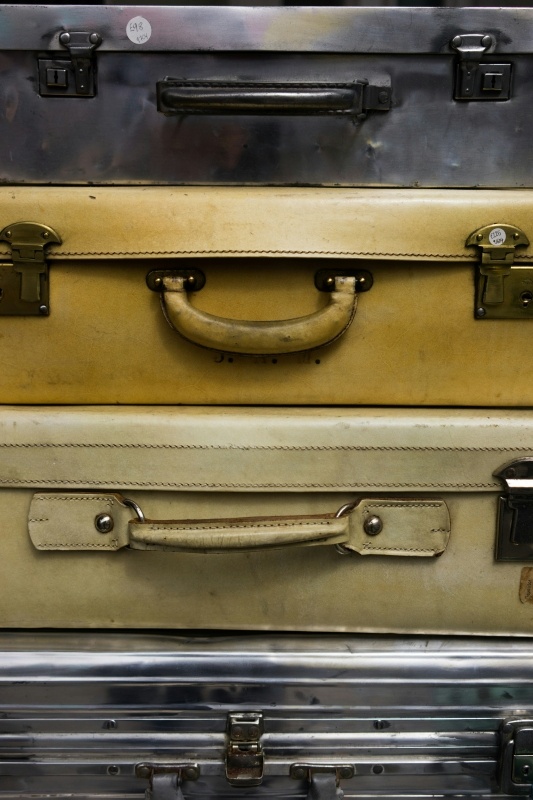 A vertical stack of four different vintage suitcases