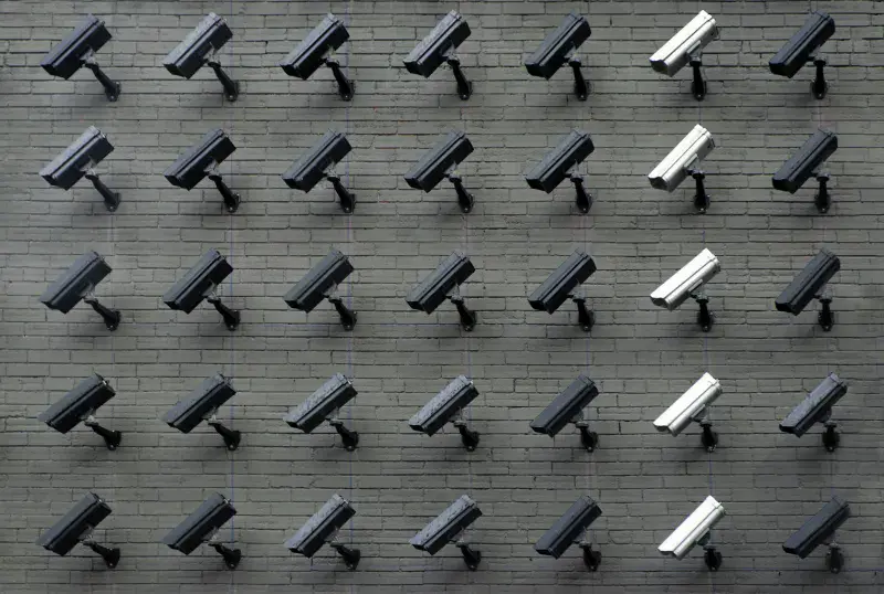 A perfect grid of identical dark CCTV cameras, with one column of cameras highlighted in a lighter colour