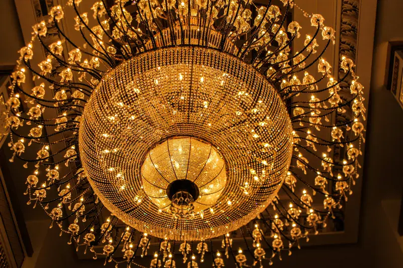 A huge, intricate golden chandelier seen from beneath, with hundreds of golden lights and sparkles