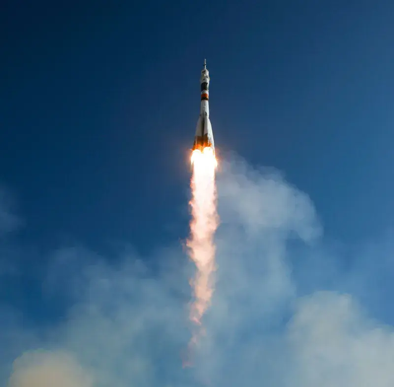 A NASA rocket launches into the blue sky, flames and smoke emanating from behind