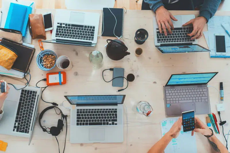 A busy hackathon table viewed from above, filled with laptops and headphones and snacks