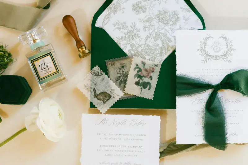 An elaborate wedding invitation laid out, with custom envelope, ribbons and fragrance bottle