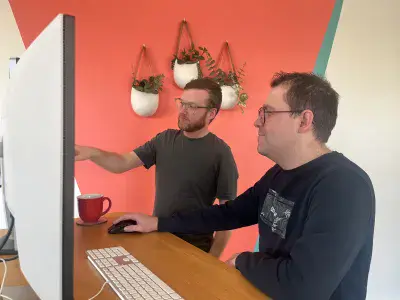 Two web developers stand at a desk and solve a problem together on the screen