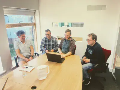 Web developers sitting around a large meeting room table, looking at a laptop together