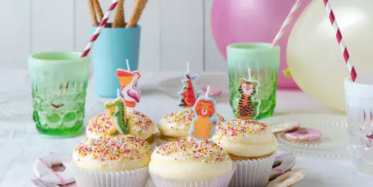 Image of a kids party table set up.  In the forefront is a plate of 5 cupcakes with animal candles in them. 