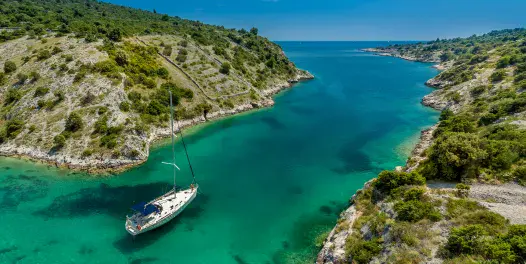 Sailboat anchored in a turquoise bay surrounded by rocky, green hills under a clear blue sky.